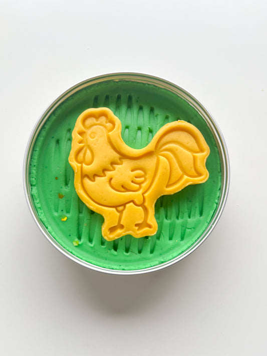Green playdough in tin with grass print featuring a yellow cockrel topper for party bag fillers for farm animal themed kids birthday parties
