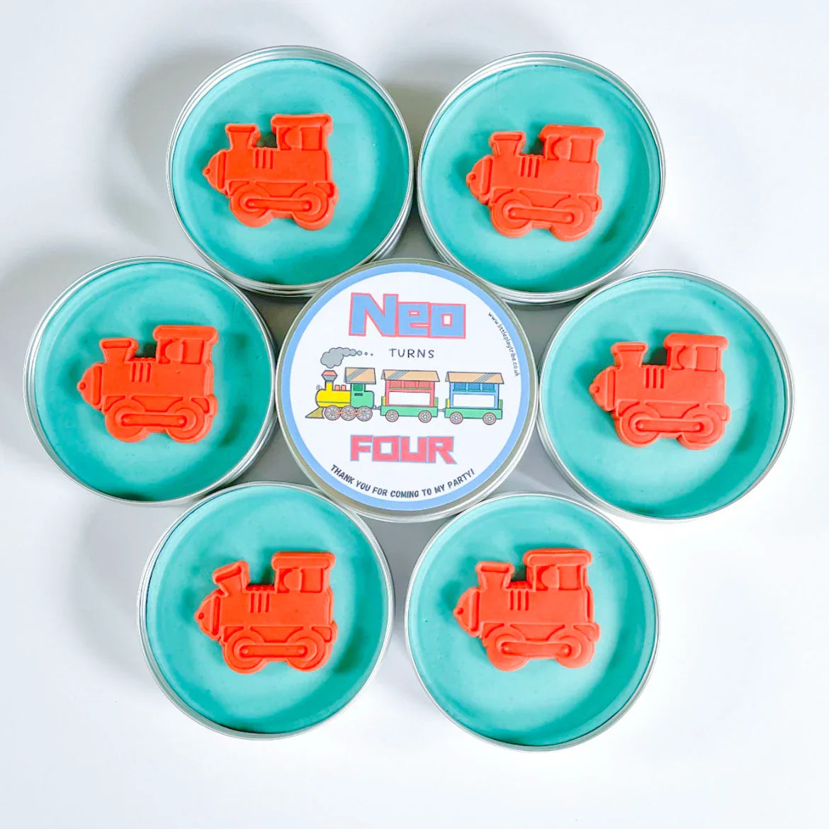 Train party bag fillers. Tins of blue playdough with red cut out train shaped playdough toppers. Personalise Neo turns 4 party bag filler label in the middle