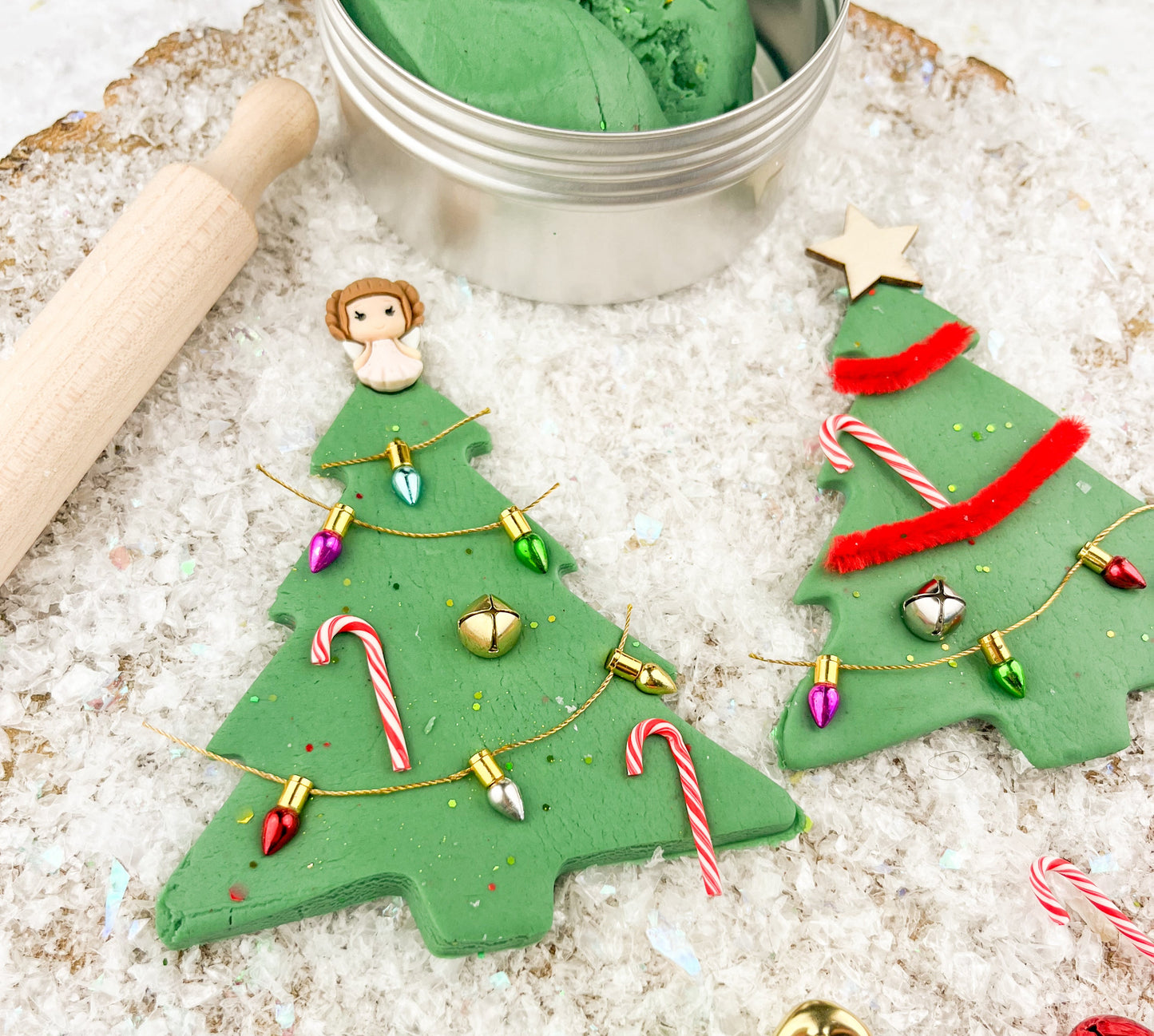 Green play dough shaped like Christmas trees with decorations on a textured surface.