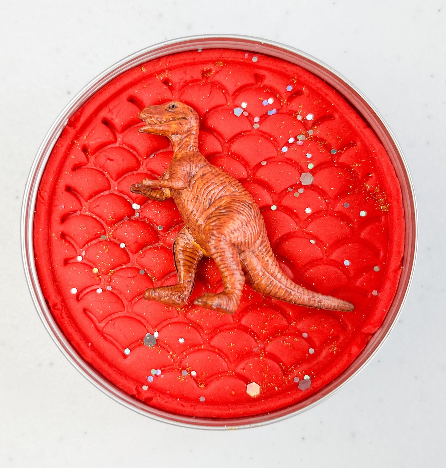 Red round playdough container with a dinosaur figure on a white background