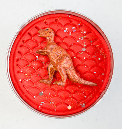 Red round playdough container with a dinosaur figure on a white background
