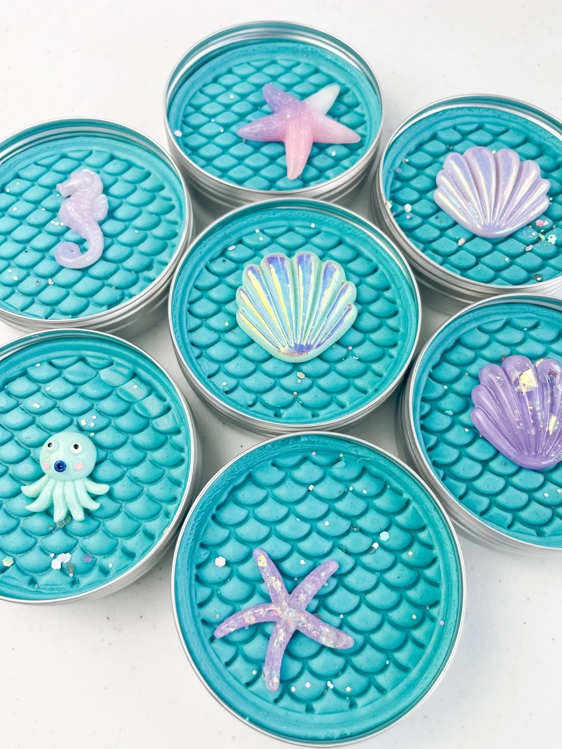 Tins of Blue playdough with mermaid scale inprint for mermaid and under the sea themed kids birthday party favours. Alternative party bag filler with under the sea resin charms