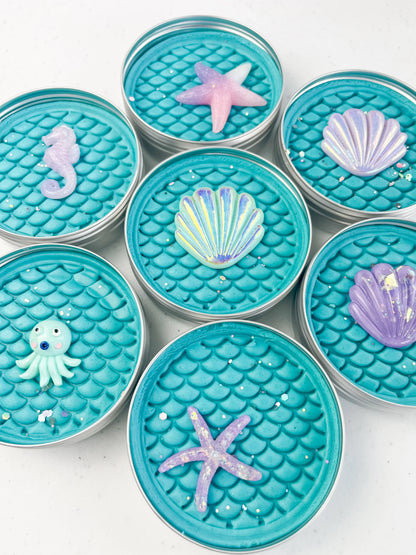 Tins of Blue playdough with mermaid scale inprint for mermaid and under the sea themed kids birthday party favours. Alternative party bag filler with under the sea resin charms