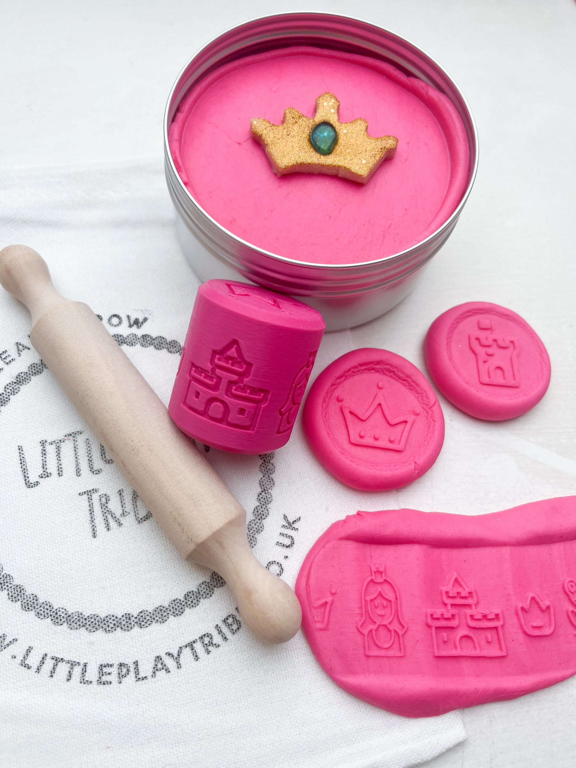 Pink Playdough in 250g maxi tub size in princess theme with hidden princesses, topped with a gold glitter crown. Shown as a grab and go dough set with Little PlayTribe Bag, Eco Princess Roller and Wooden Rolling Pin for Playdough accessories and dough tools. Playdough kit