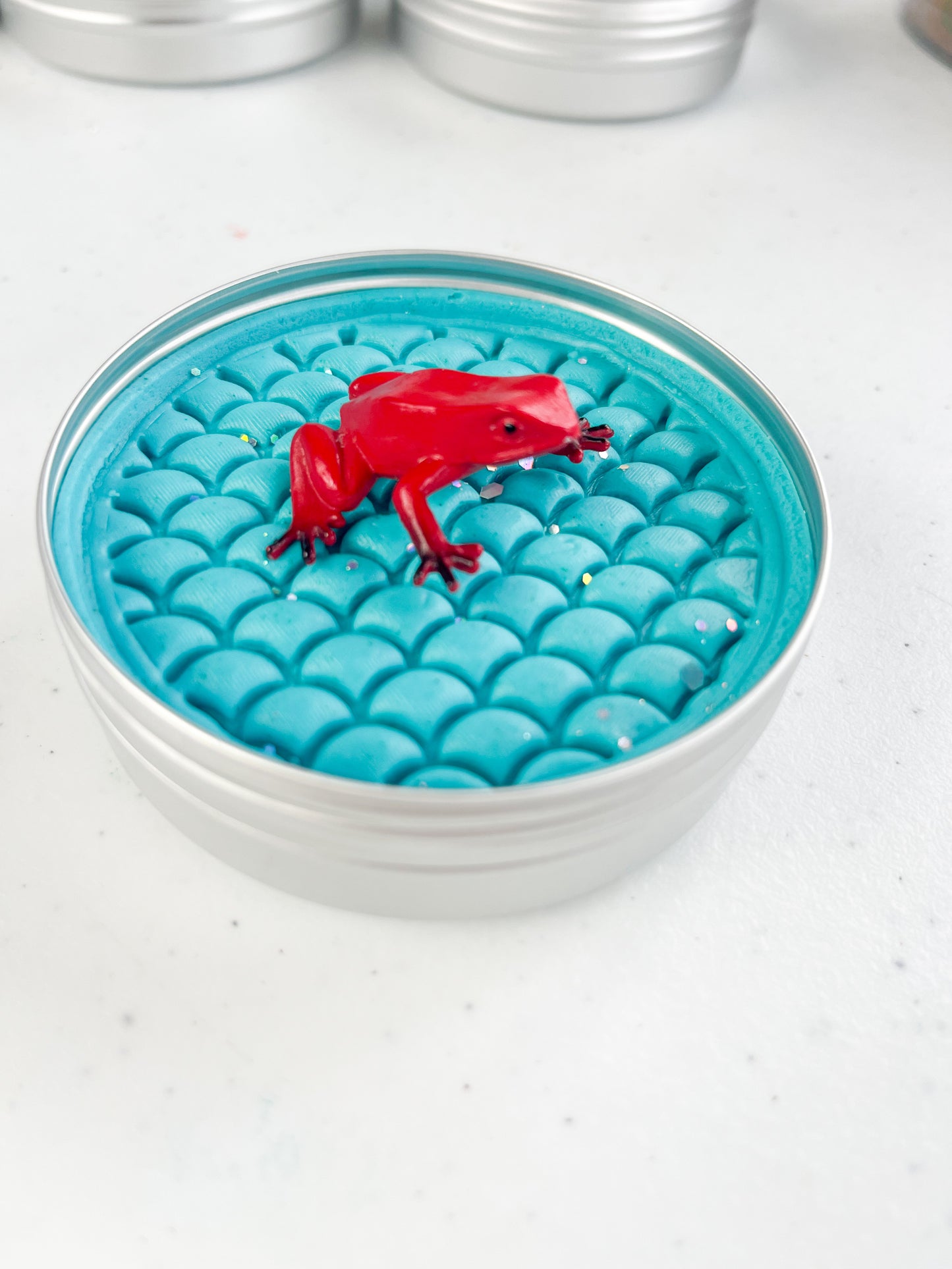 Reptile Themed Sensory Playdough Pots for Alternative Party Bag Fillers. Eco friendly, handmade playdough in a mix of colours with reptile animal characters on top. Blue plsydough pot with red frog figure on top
