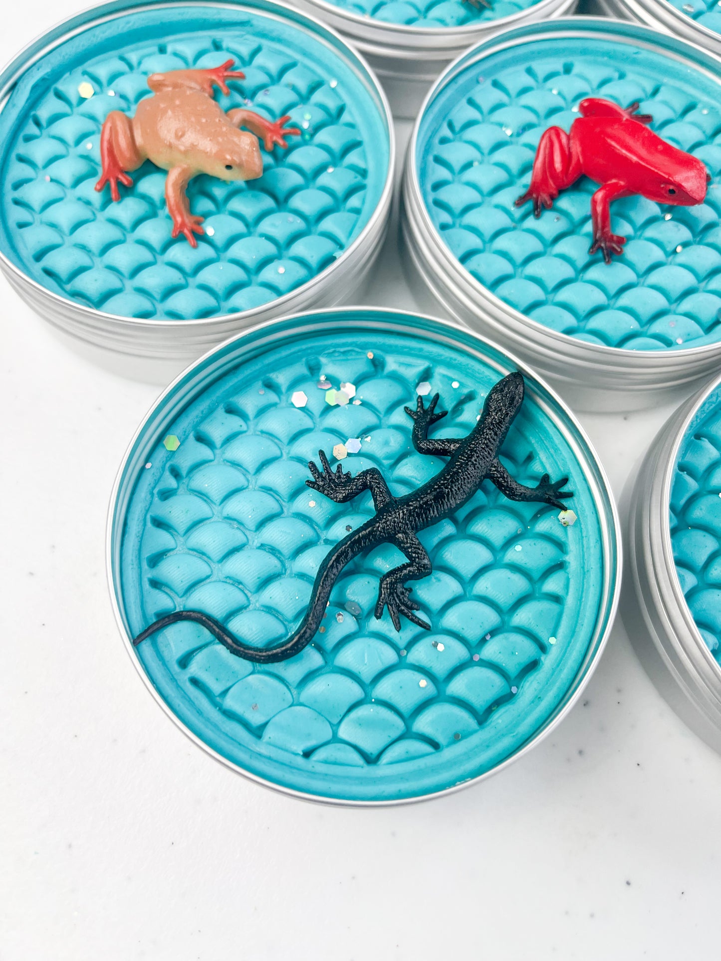 Reptile Themed Sensory Playdough Pots for Alternative Party Bag Fillers. Eco friendly, handmade playdough in a mix of colours with reptile animal characters on top. Set of blue playdough pots with various reptile figures on top