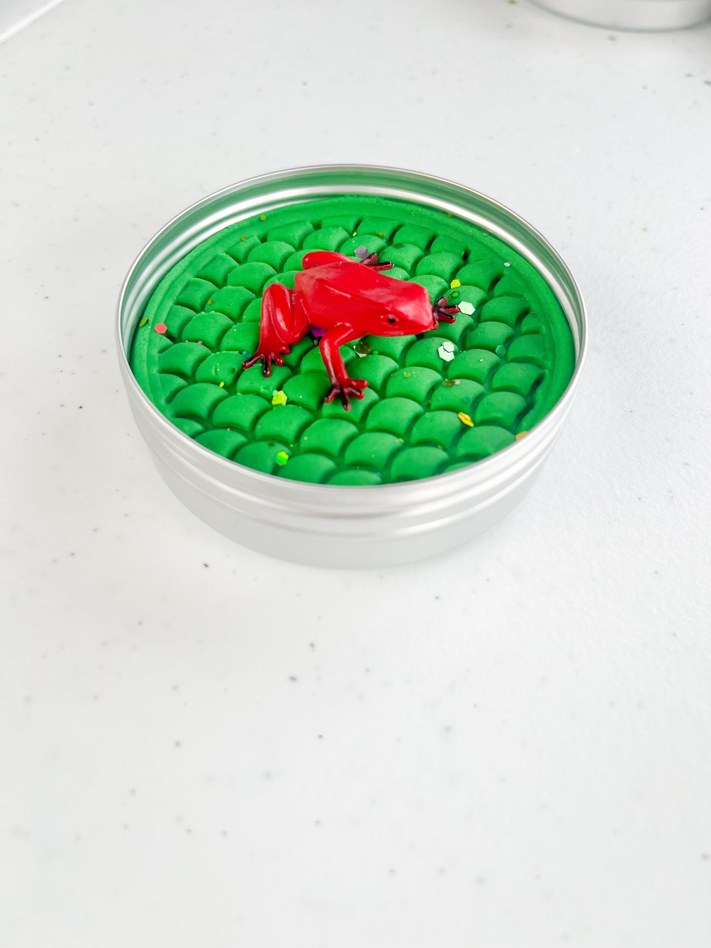 Reptile Themed Sensory Playdough Pots for Alternative Party Bag Fillers. Eco friendly, handmade playdough in a mix of colours with reptile animal characters on top. One tine of green playdough with frog figure on top