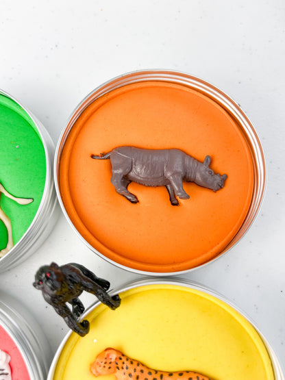 Safari Animal Themed Sensory Playdough Pots for Alternative Party Bag Fillers. Eco friendly, handmade playdough in a mix of colours with safari animal characters on top. Set of primary coloured playdough pots with various animal figures on top. Orange Playdough in metal tub with rhino figure on top.